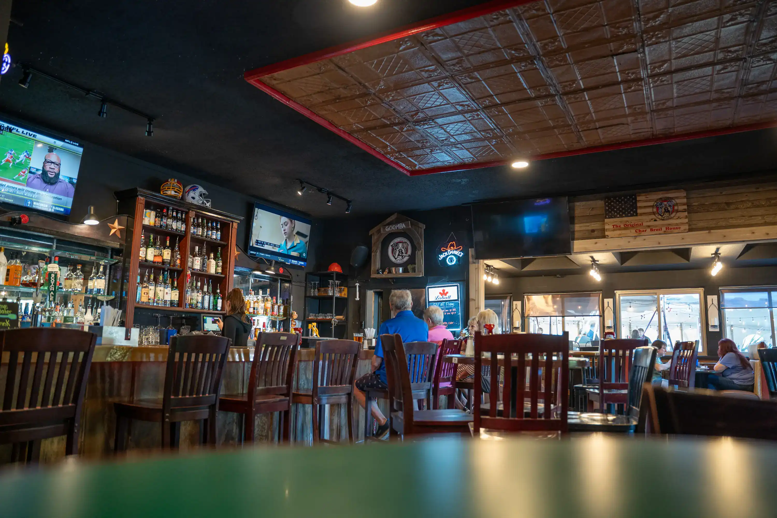 Bar area with wooden chairs, liquor shelves, and sports TVs at The Original Charbroil House