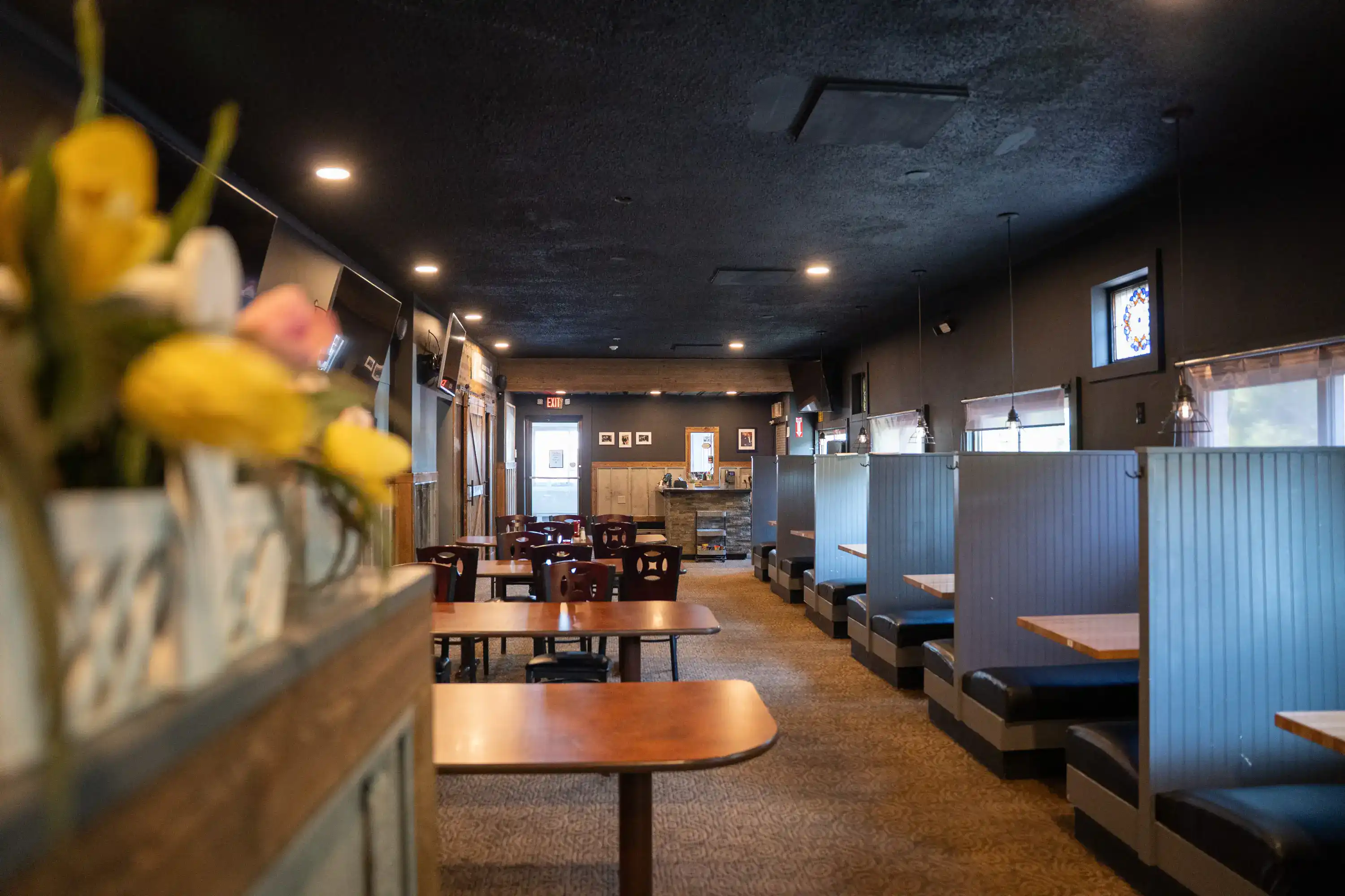Restaurant dining room with dark blue booth seating, wooden tables, and black ceiling