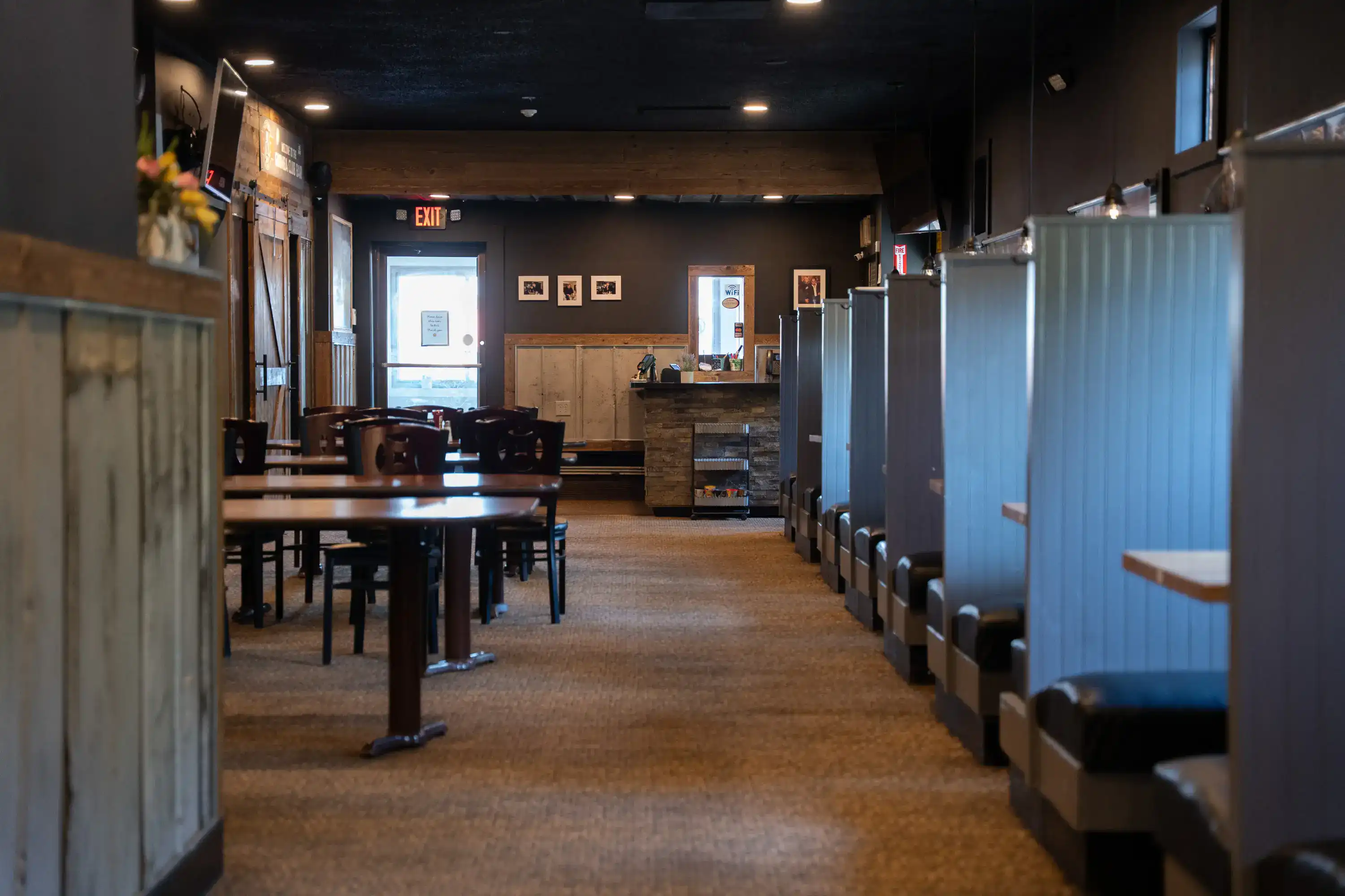 Restaurant dining room with dark walls, wooden tables, and blue corrugated metal booths
