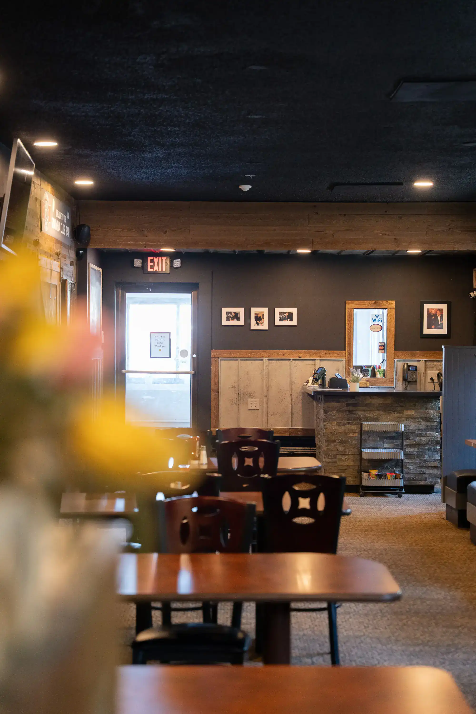 Restaurant dining area with dark ceiling, wood accents, and service counter near exit