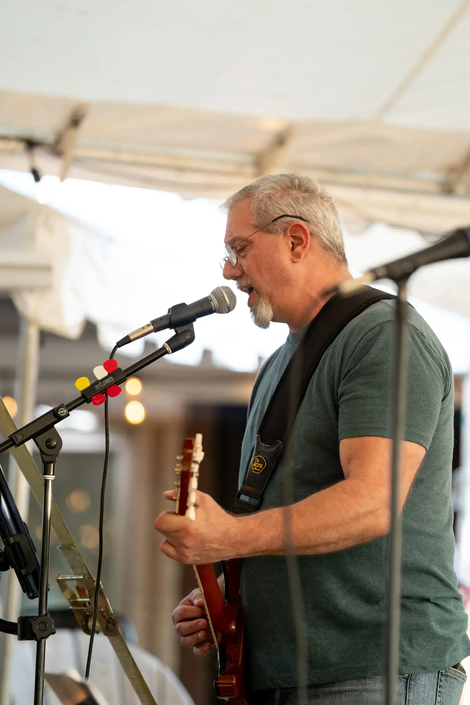 Musician with guitar and goatee performing at microphone under white tent