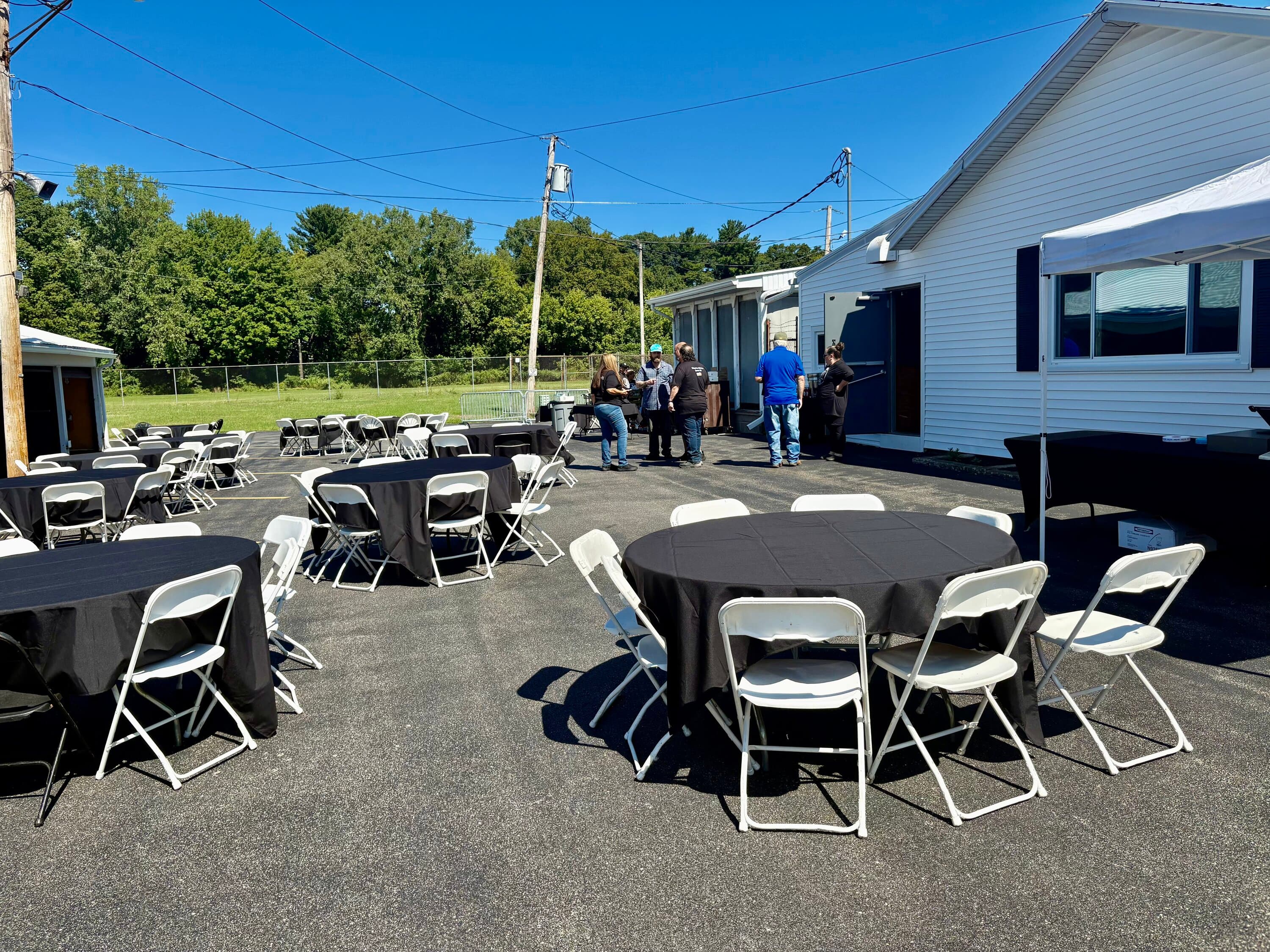 Round tables with black tablecloths and white folding chairs set up for outdoor event