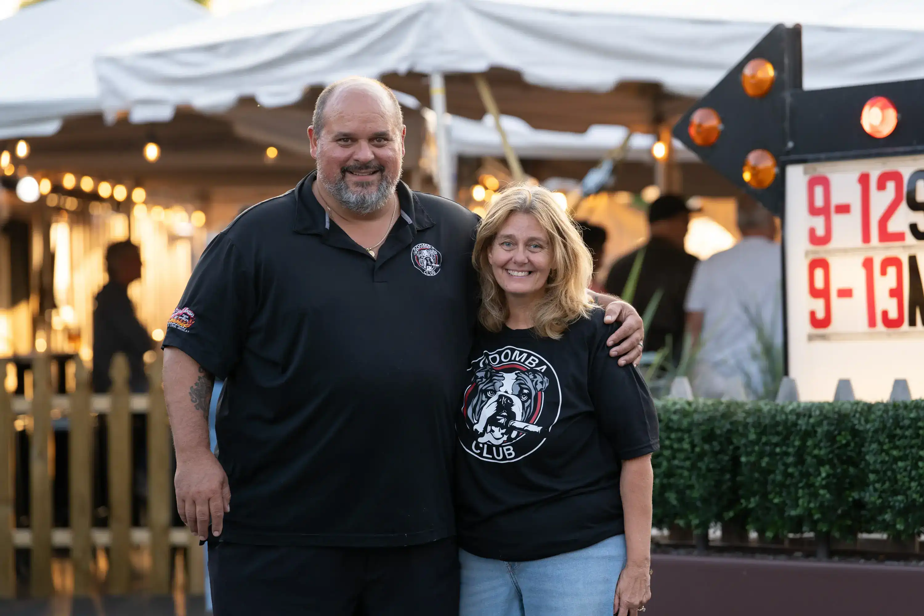 Two owners wearing Goomba Club shirts standing in front of outdoor restaurant venue