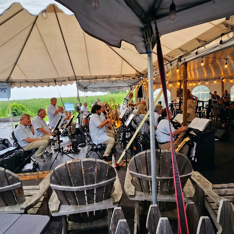 Live swing band performs under a tent beside an outdoor dining area filled with wooden chairs and guests.